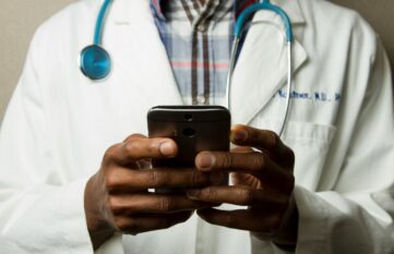 Person im Arztkittel mit grünem Stethoskop am Hals mit Telefon
